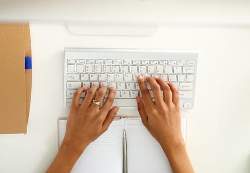 Hand of black woman type something with white wireless computer keyboard closeup