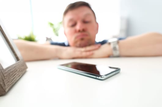 Cellphone lying on table with pensive man in background waiting for call or out of network coverage closeup