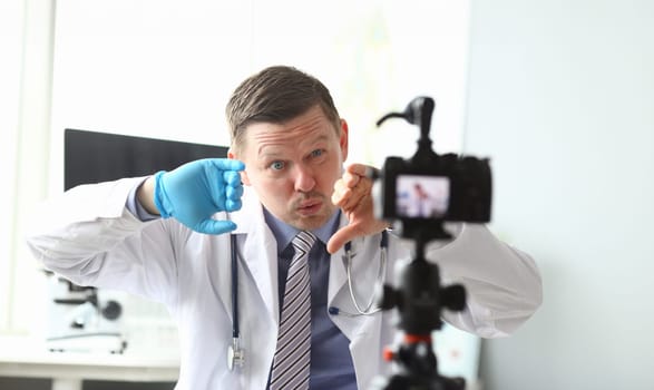 Male vlogger doctor look at camera aganist hospital office background. Online consultation patient concept