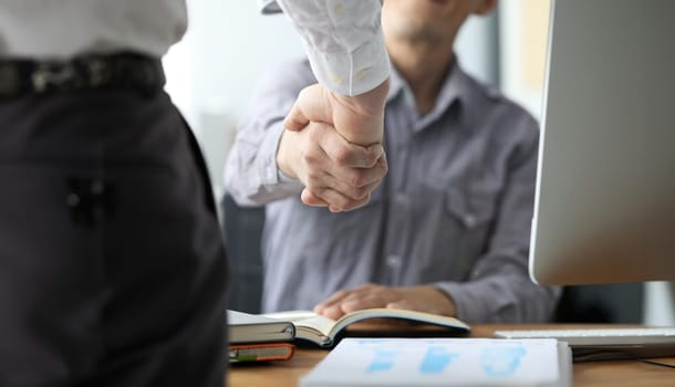 Focus on men shaking hands in office. Boss hiring new stuff for work. Businessman sitting by table greeting male wearing formal clothes. Meeting of partners and agreement on deal