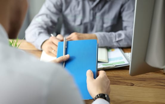 Focus on notebook and pen in hands of man at job meeting or interview. Candidate holding book and sitting with boss by table. Businessman writing info in handbook. Recruitment or negotiations