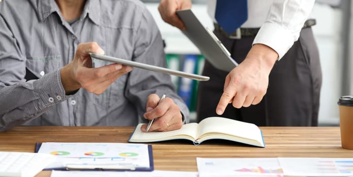 Close-up of male hands holding modern tablet and documents. Colleagues discussing important statistics data of new project and writing something in notepad. Business concept