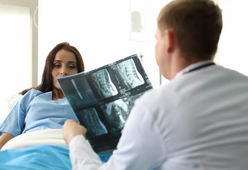 Portrait of beautiful woman discussing important results of x-ray of back with therapist. Lovely lady lying in hospital ward. Healthcare and treatments concept