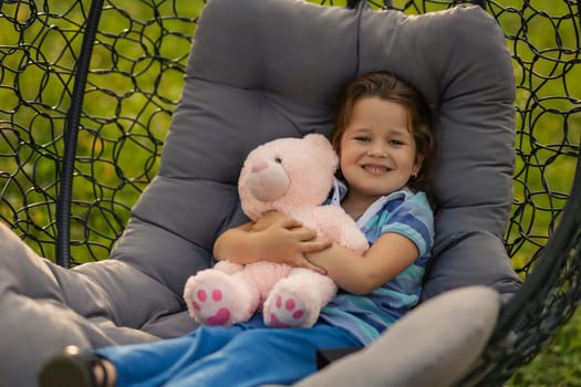 child hugging a teddy bear while sitting in a hanging chair