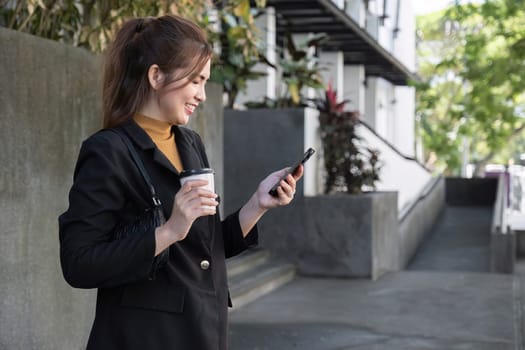 Attractive smiling Asian businesswoman wearing a suit standing in the city using an application on her mobile phone Read news on your smartphone fast connection Check out the outdoor mobile app.