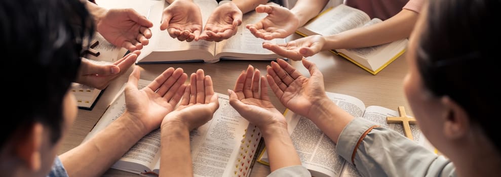 Cropped image of diversity people hand praying together at wooden church on bible book. Group of believer hold hand together faithfully. Concept of hope, religion, faith, god blessing. Burgeoning.