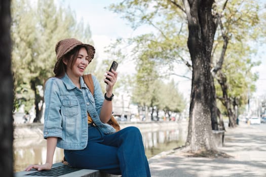 Young Asian tourist walking along city streets and holds a mobile phone on the pavement.