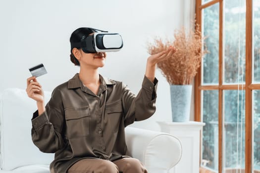 Young woman using virtual reality VR goggle at home for uttermost online shopping experience. The virtual reality VR innovation optimized for digital entertainment lifestyle.