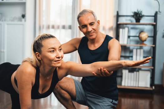 Happy active senior couple in sportswear being supportive and assist on yoga posture together at home. Healthy senior man and woman lifestyle with yoga exercise. Clout