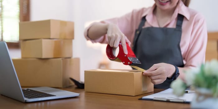 Woman use scotch tape to attach parcel boxes to prepare goods for the process of packaging, shipping, online sale internet marketing ecommerce concept startup business idea.