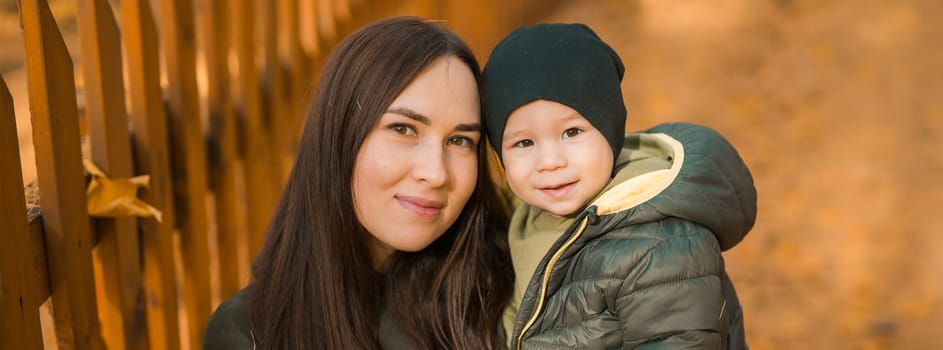 Cute little boy stands with mother outdoors. Happy child walking in autumn park. Toddler baby boy wears trendy jacket and hat. Autumn fashion. Stylish child outside