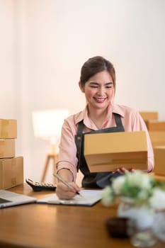 Young woman working online ecommerce shopping at her shop. Young woman sell prepare parcel box of product for deliver to customer. Online selling, ecommerce. Selling products online.