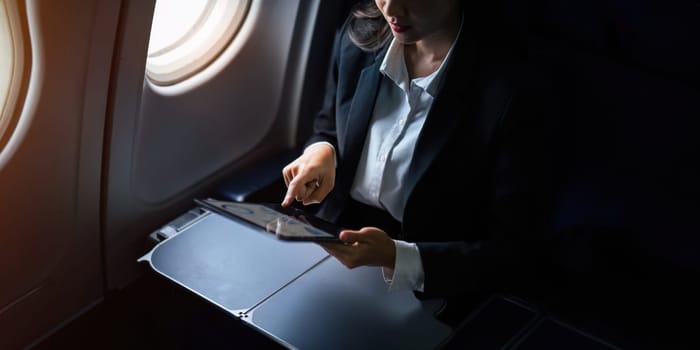 Successful Asian business woman, Business woman working in airplane cabin during flight on tablet.