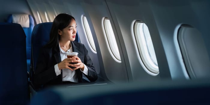 Successful Asian business woman, Business woman working in airplane on laptop computer and looking out the window.