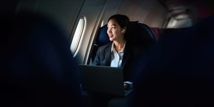 Successful Asian business woman, Business woman working in airplane cabin during flight on laptop computer listening to music with headphones.