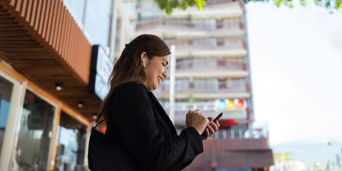 Asian professional businesswoman holding cellphone using smartphone standing or walking on big city urban street outside. Successful Asian business woman.