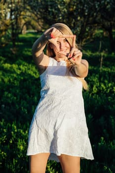 a woman in a white dress in a blooming garden in a park in nature journey walking shows a square with her fingers