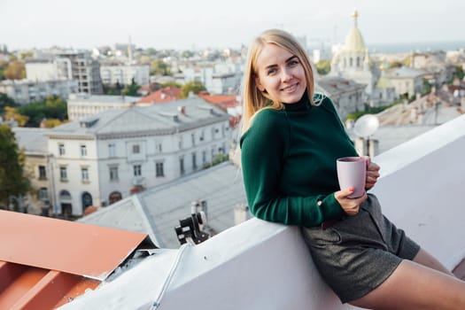 blonde beautiful woman with a mug on the roof of a house on the street