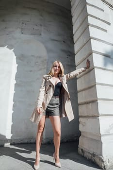 blonde fashionable woman in a raincoat stands against the wall outside walk rest