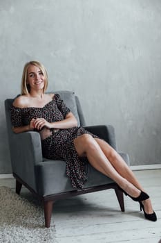 beautiful blonde woman in summer clothes sitting in chair on the room