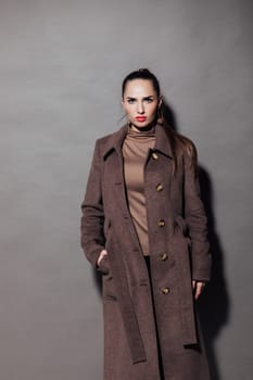 fashionable and beautiful woman in a brown cape stands on a gray background