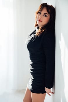 a woman in black dress stands against a white wall in a room