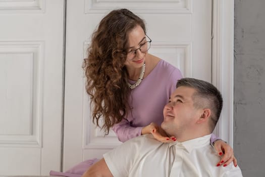 Young happy couple sitting on a sofa in a large studio. Behind them is a large white door. Loving married couple. Cope space for text