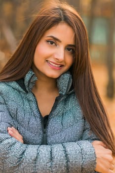 Close-up portrait of a young beautiful confident Indian Asian woman in fall outdoor. Happy and natural smiling female. Generation z and gen z youth