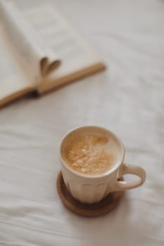 Cozy morning composition with a coffee cup and a book with pages folded into a heart shape in bed.