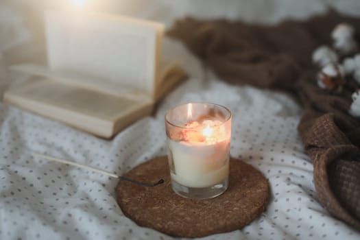 Cozy still life interior details with a book, candle and a cotton flower in warm soft bed. Sweet home