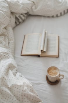Cozy morning composition with a coffee cup and a book with pages folded into a heart shape in bed.