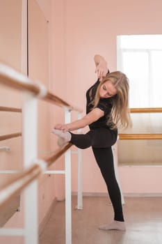 Caucasian blonde woman is practicing ballet in class. A ballerina rehearses at the barre. Vertical photo