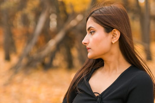 Close-up portrait of a young beautiful confident Indian Asian woman in fall outdoor. Happy and natural smiling female. Generation z and gen z youth