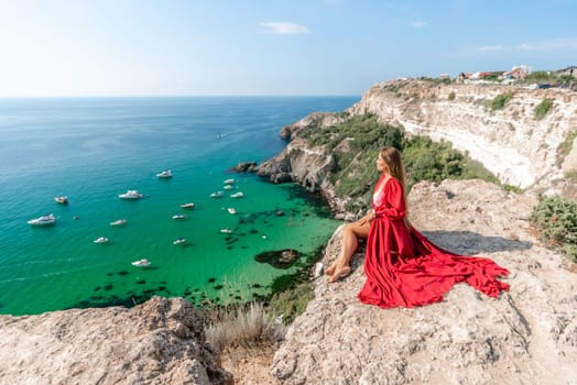 Woman red dress sea. Happy woman in a red dress and white bikini sitting on a rocky outcrop, gazing out at the sea with boats and yachts in the background