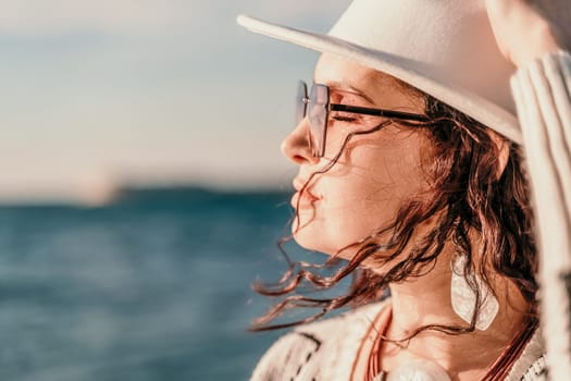 Portrait of a curly haired woman in a white hat and glasses on the background of the sea. Vacation on the sea, walk, tourism