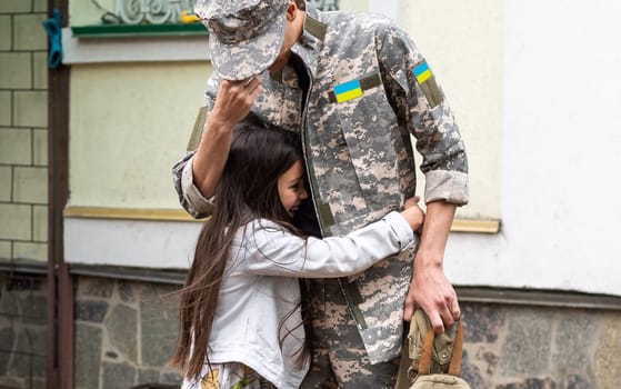 Soldier in Ukrainian military uniform hugging his daughter. Family reunion.