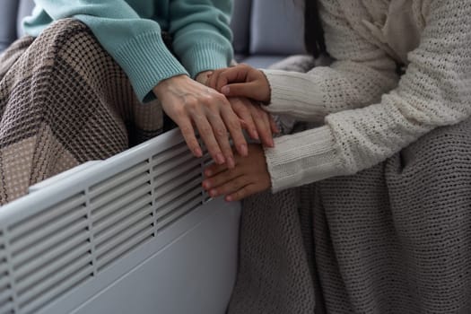 Mother and child warming hands near electric heater at home, closeup