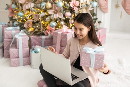 teenage girl works at home remotely with laptop on the background of a Christmas tree. Quarantine, work on holidays. atmosphere and work at home.