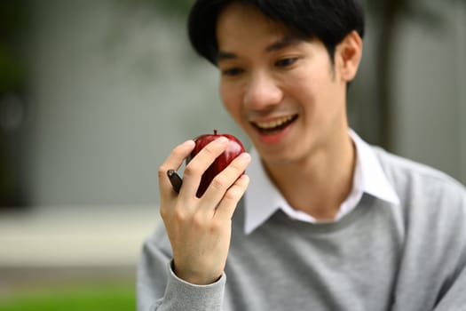 Happy asian man student eating apple during break in campus. People, education and lifestyle.