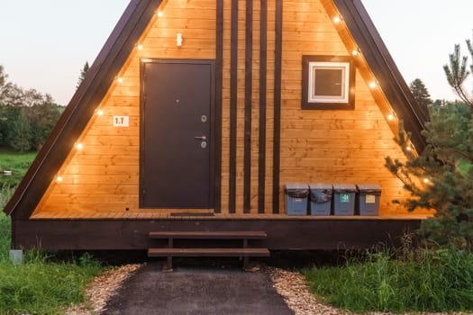 The concept of glamping and renting a chalet for weekend. Wooden house with a veranda in nature around coniferous trees.