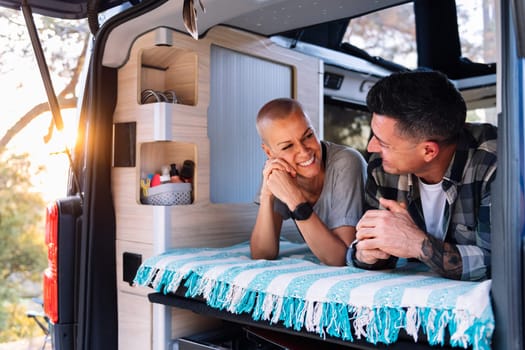 happy couple relaxing lying in the back of their camper van, concept of active tourism in nature and outdoor activities