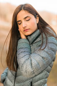 Close up portrait of pretty indian young woman closed eyes enjoying warm autumn sunny day vacation outdoors. Generation z and gen z concept. Fall Season.