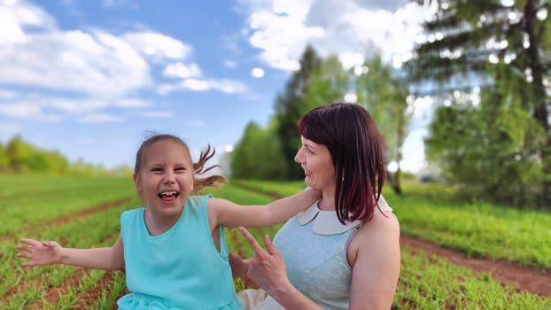 Happy mother and daughter enjoying rest, playing and fun on nature in green field. Woman and girl resting outdoors in summer or spring day