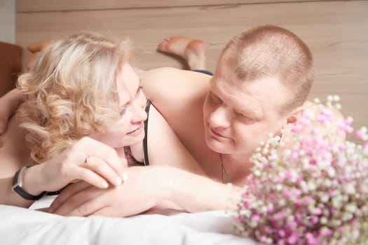 Loving enamored adult couple communicates, embraces, and has fun alone together on the bed in the bedroom or hotel room. The woman is wearing tank top and the man is shirtless