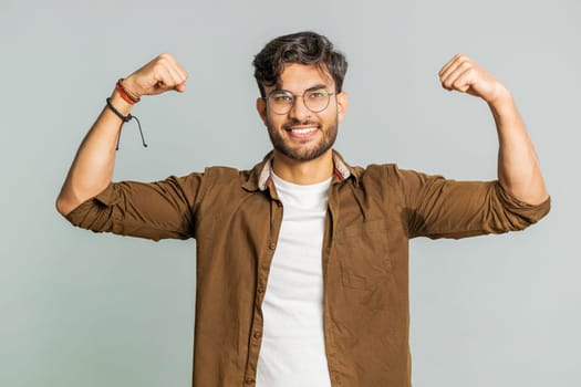 I am strong and independent. Young Indian man showing biceps and looking confident, feeling power strength to fight for rights, energy to gain success win. Guy isolated on gray studio background