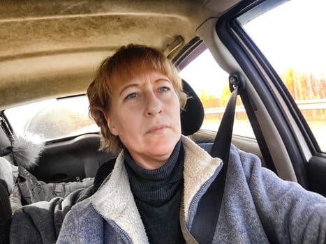 Portrait of female driver in solo journey. Adult mature woman holding steering wheel and looking through windscreen in travel by vehicle on vacation. Lady girl who is owner or rent car for travel