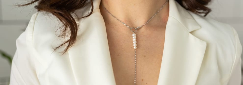 Close up of a beautiful elegant young woman wearing an expensive pearl necklace in a white blazer.