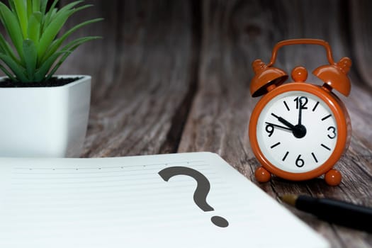 Question mark on notepad alarm clock on wooden background. Q and A concept.