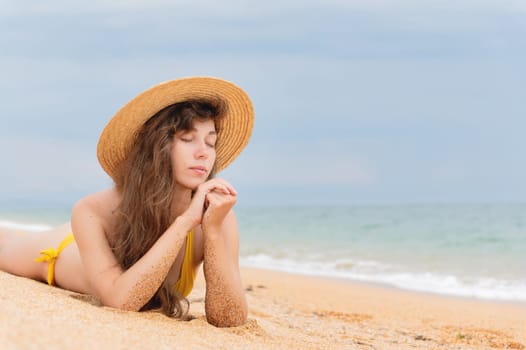 Summer lifestyle. Portrait of a beautiful girl with a slim body in a bikini enjoying life and lying with her eyes closed on the sand on the beach of a tropical island. Vacation.