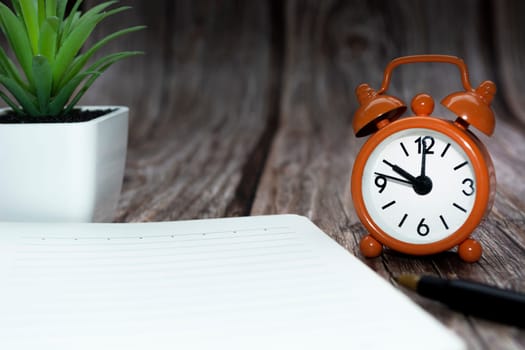 Notepad with potted plant and alarm clock set at 10 o'clock against wooden background. Business concept. Copy space.